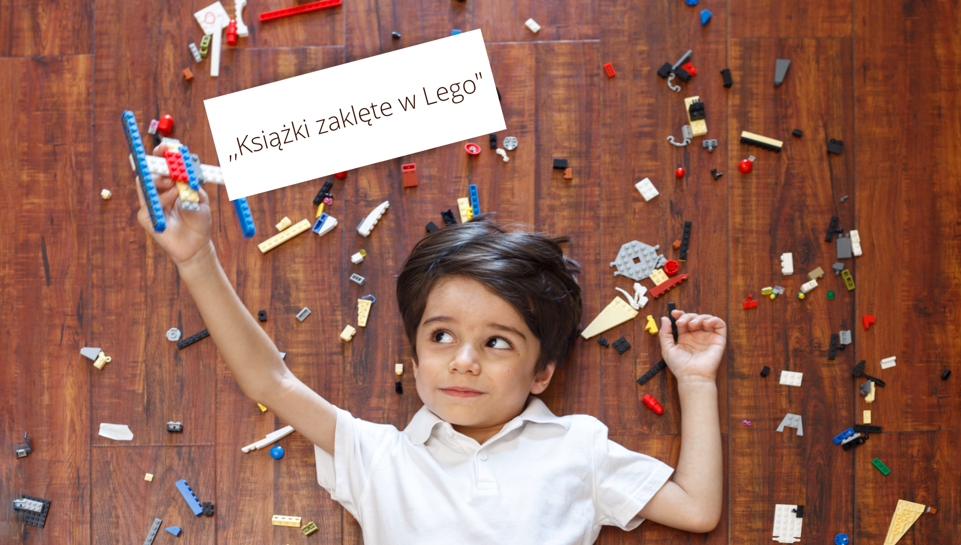 Chłopiec leży na podłodze wśród kolorowych klocków Lego i trzyma w prawej, uniesionej do góry ręce, zrobiony z nich samolocik. U góry napis ,,Książka zaklęta w Lego".