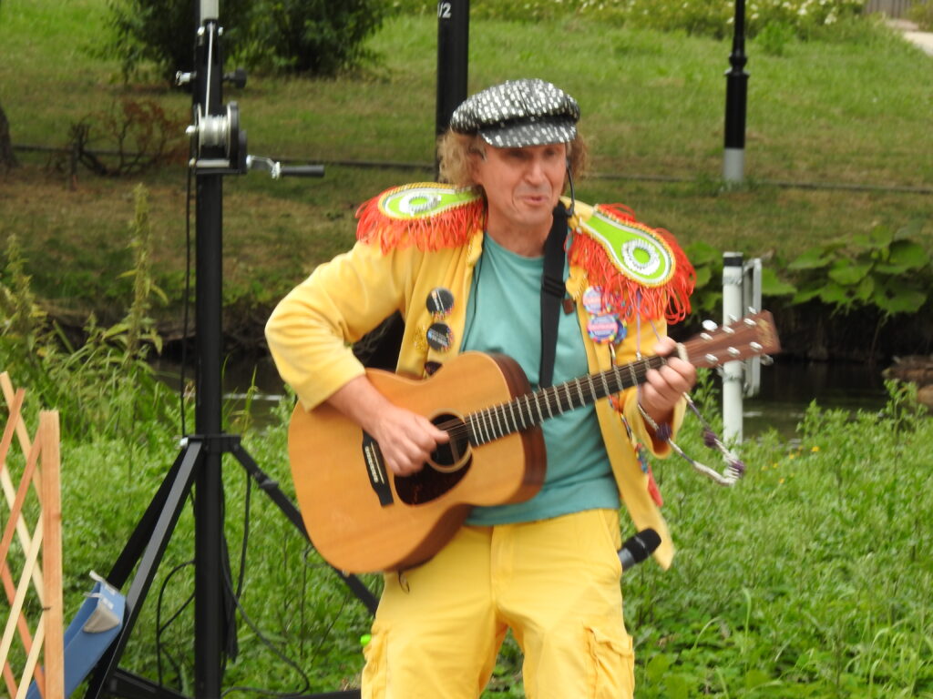 Mężczczyzna w żółtym stroju na świzym powetrzu. W rękach trzyma gitarę.