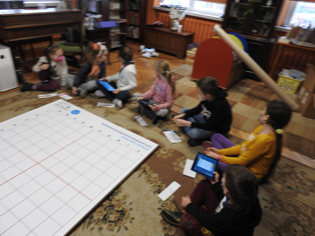 na dywanie mata z napisem: kodowanie na dywanie, wokół niej siedzą dzieci.