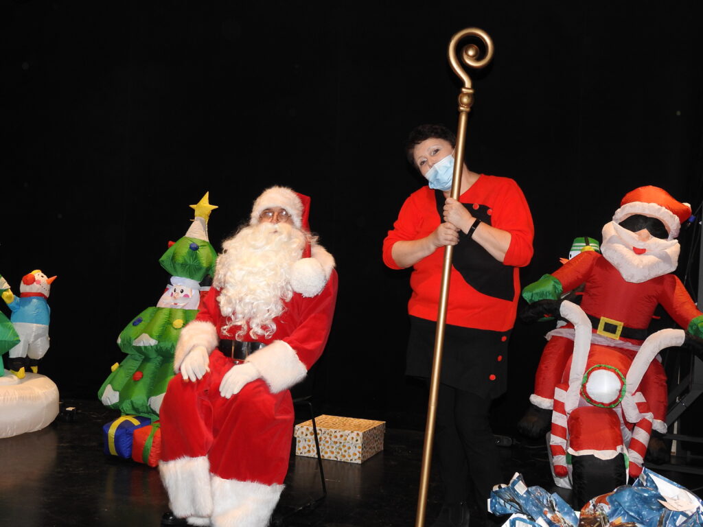 Święty Mikołaj oraz postać stojąca obok z laską Mikołaja. Za nimi dmuchane ozdoby: choinka oraz Mikołaj na motorze.