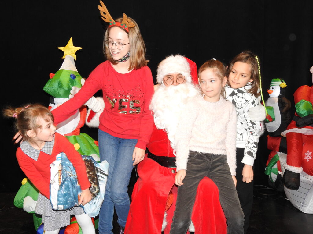 Święty Mikołaj i czwórka dzieci. Jedna dziewczynka siedzi na kolanach u Mikołaja.