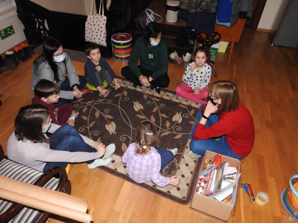 Czworo dorosłych oraz czwórka dzieci siedzi w okręgu na dywanie.