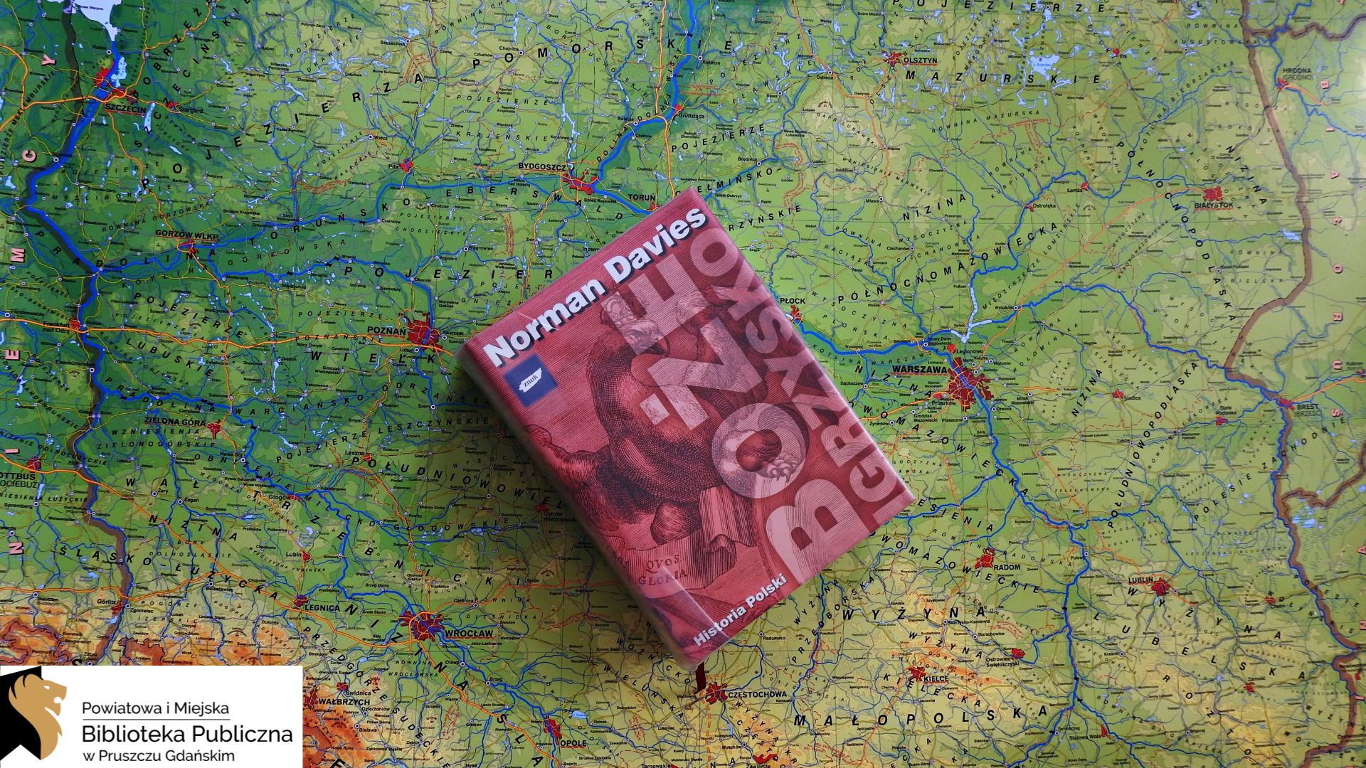 Na mapie Polski leży książka pt. Boże igrzysko. Ma bordową okładkę.