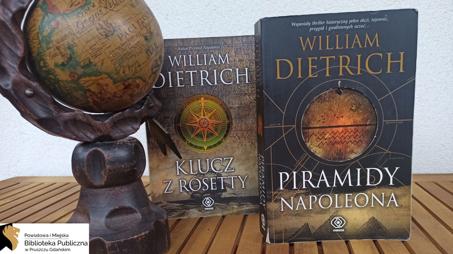 Przy starym globusie pokazującym nieaktualny obraz Ziemi stoją dwie książki: Piramidy Napoleona oraz Klucz z Rosetty.