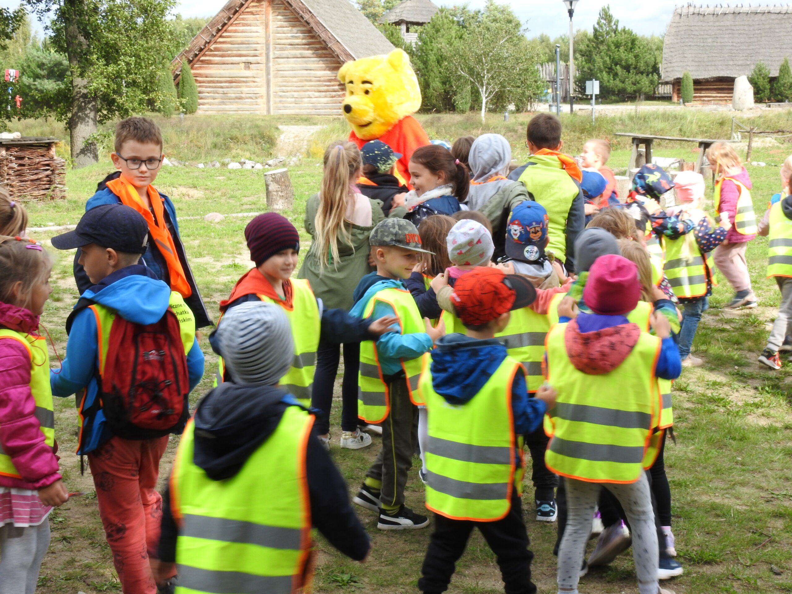 Duża grupa dzieci na świeżym powietrzu - Faktoria bawi się z maskotką Kubusia Puchatka.