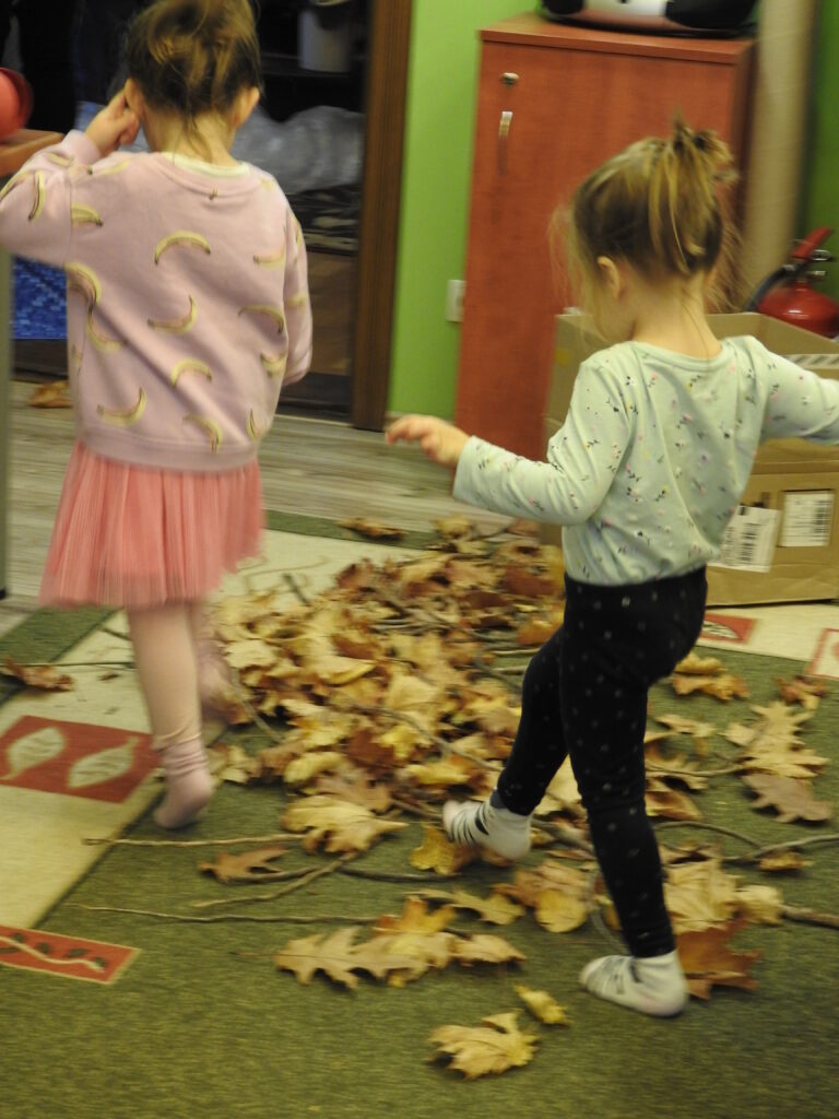 Dwoje dzieci przechodzi przez rozrzucone na dywanie liście i patyki