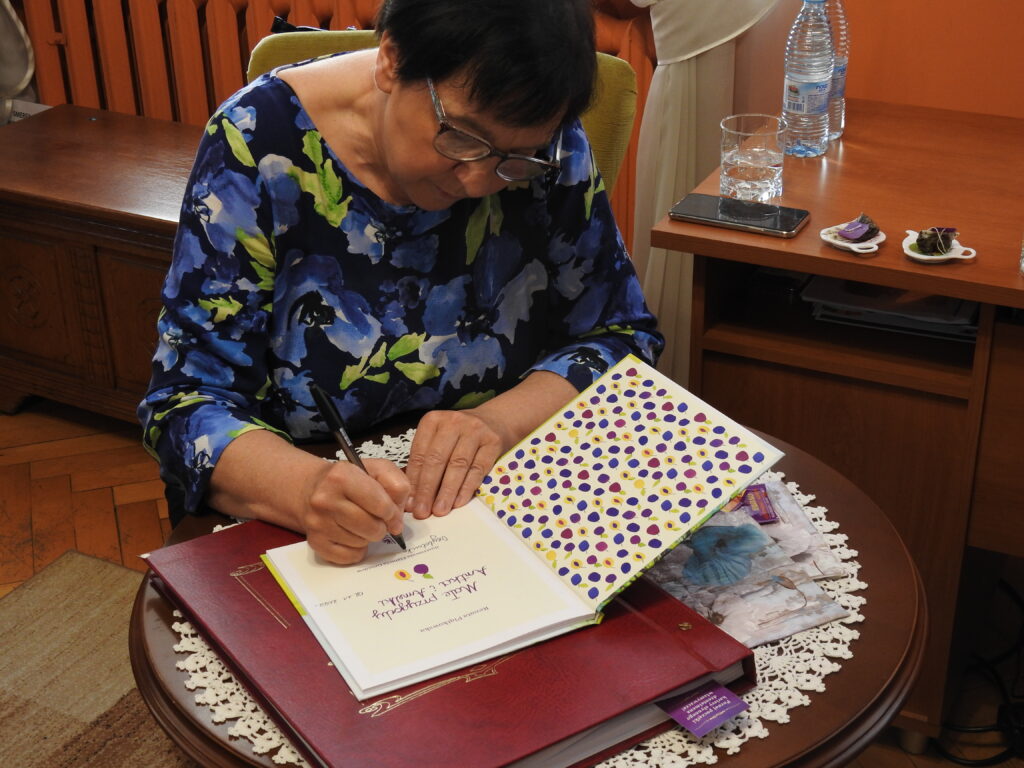 Pani Renata Piątkowska siedzi przy stoliku i podpisuje książkę.