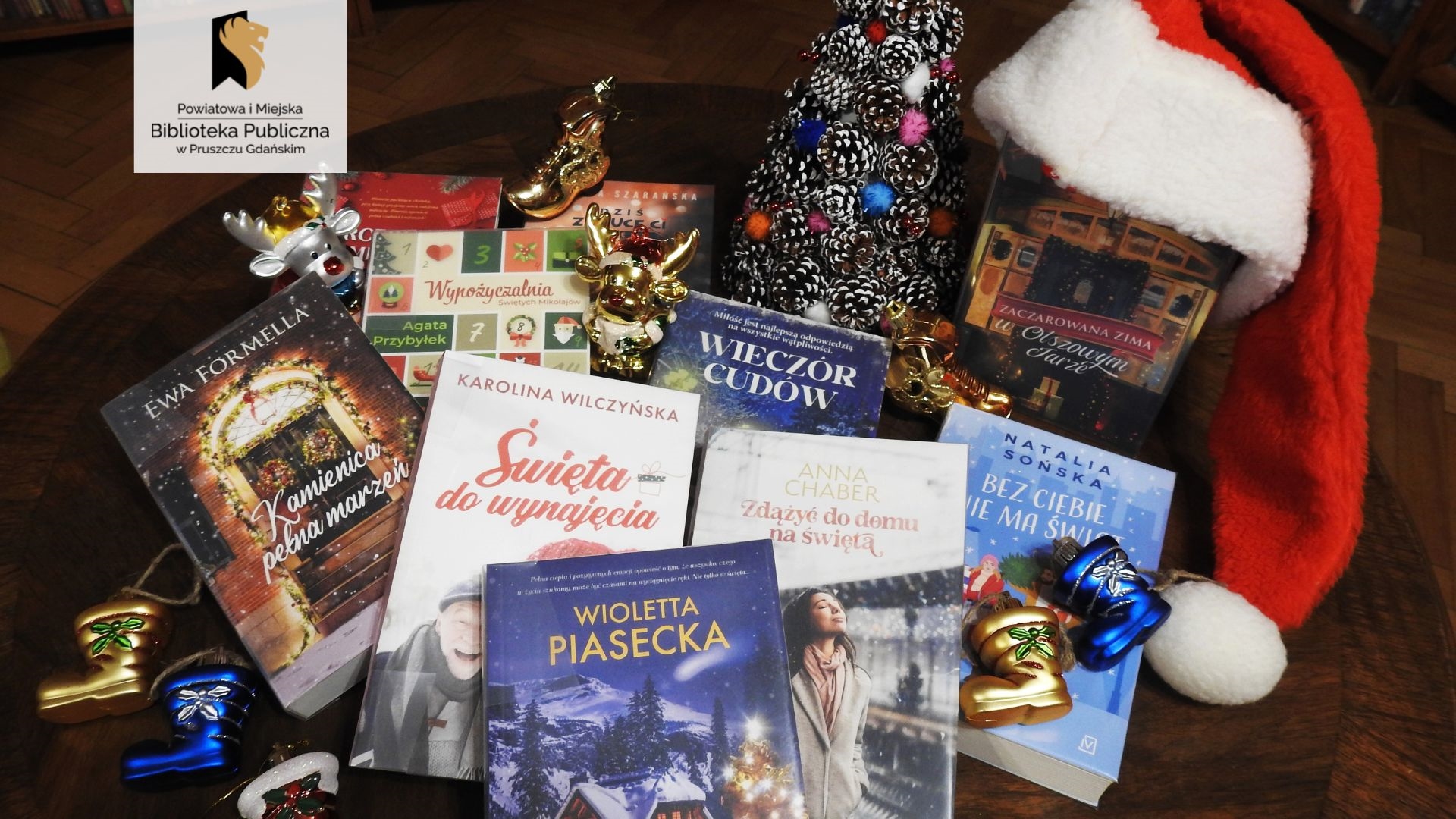 Na stoliku, wśród świątecznych ozdób: choinka, bombki, czapka Mikołaja, wyeksponowane są książki o tematyce świątecznej.