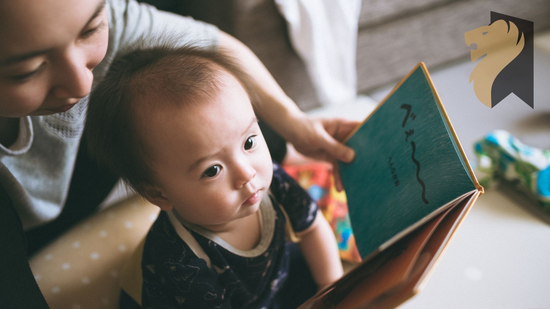 Malutkie dziecko siedzi na podłodze w o objęciach matki, która trzyma przed oczyma dziecka otwartą książeczkę.
