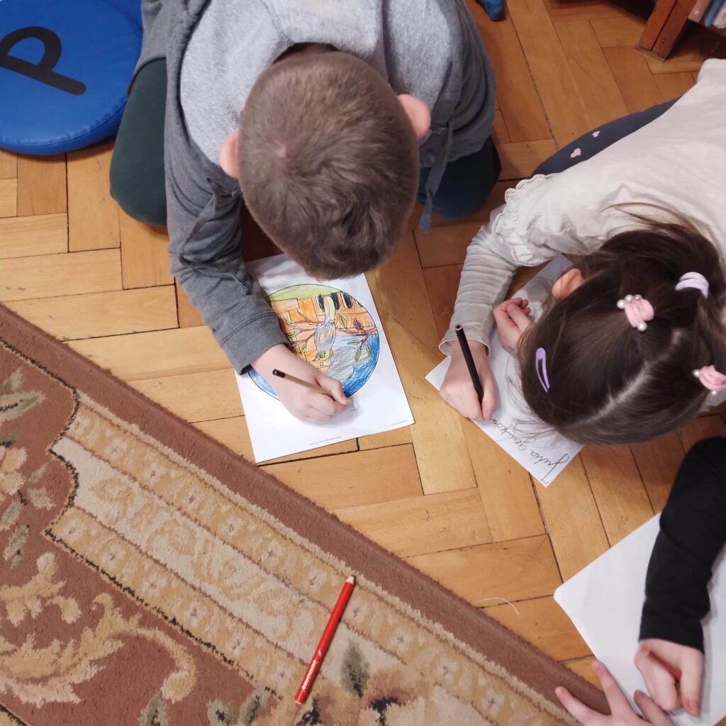Dwoje dzieci pochylonych nad kartką papieru koloruje obrazek.