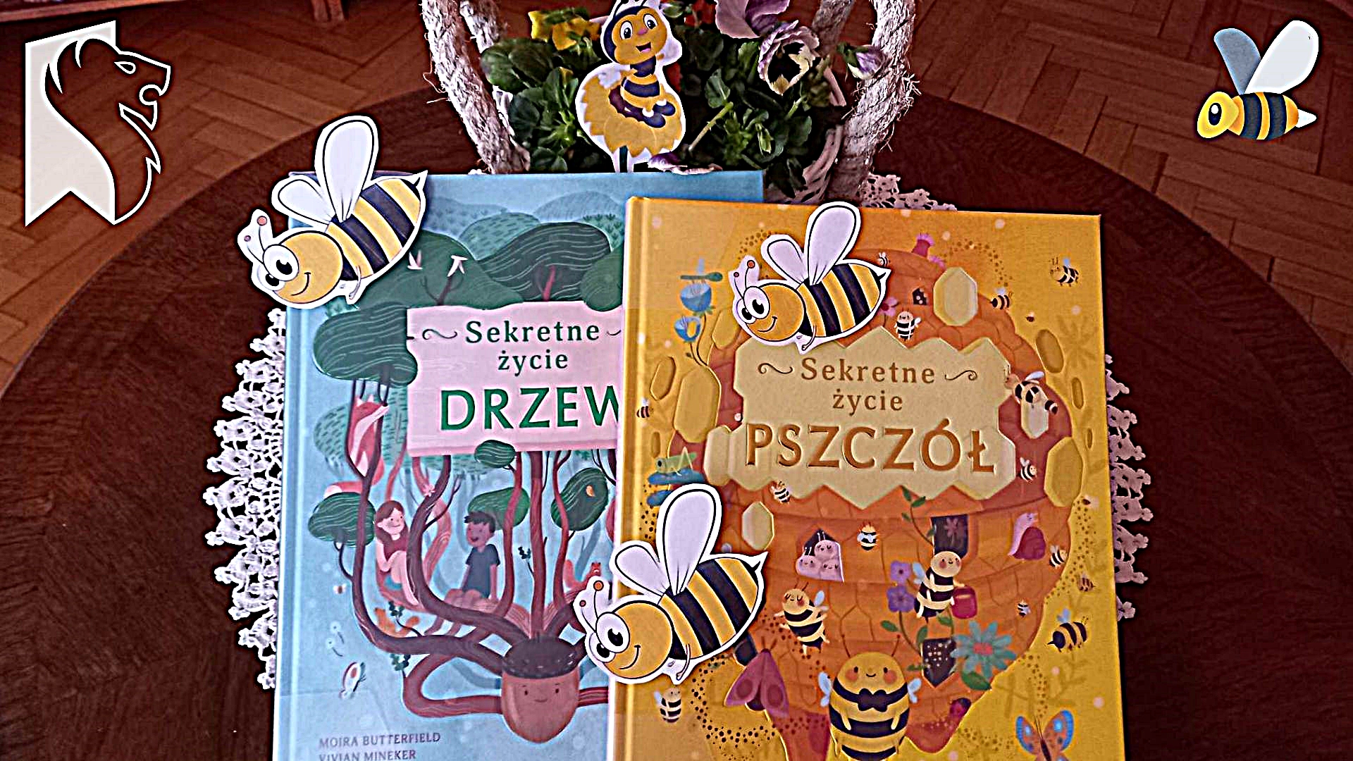 Okładki 2 książek Moiry Butterfield ,,Sekretne życie drzew" i ,,Sekretne życie pszczół". Za ksiązkami koszyk z bratkami. Na książkach oraz bratkach położone papierowe pszczółki.