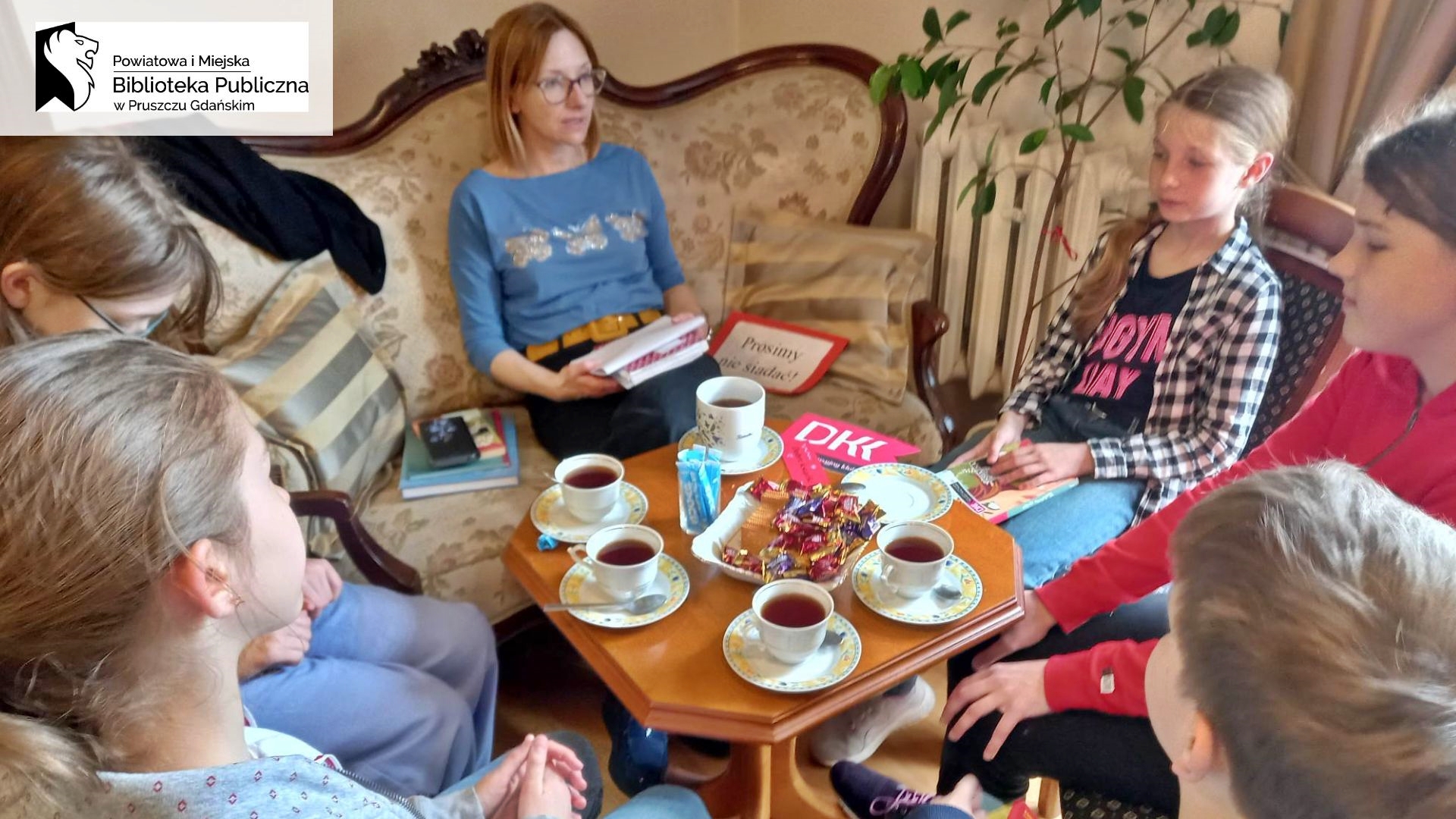 Moderatorka Dyskusyjnego Klubu Książki Joanna Łabasiewicz oraz 5 dzieci siedzą przy stoliku i rozmawiają o książce.