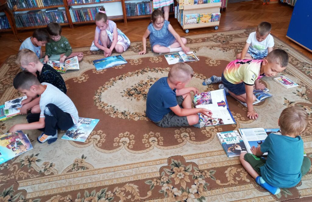 Dzieci siedzą na dywanie. Przed sobą maja położone książki.