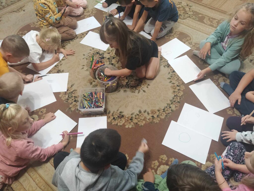 Dzieci siedzą w okręgu na podłodze i rysują.