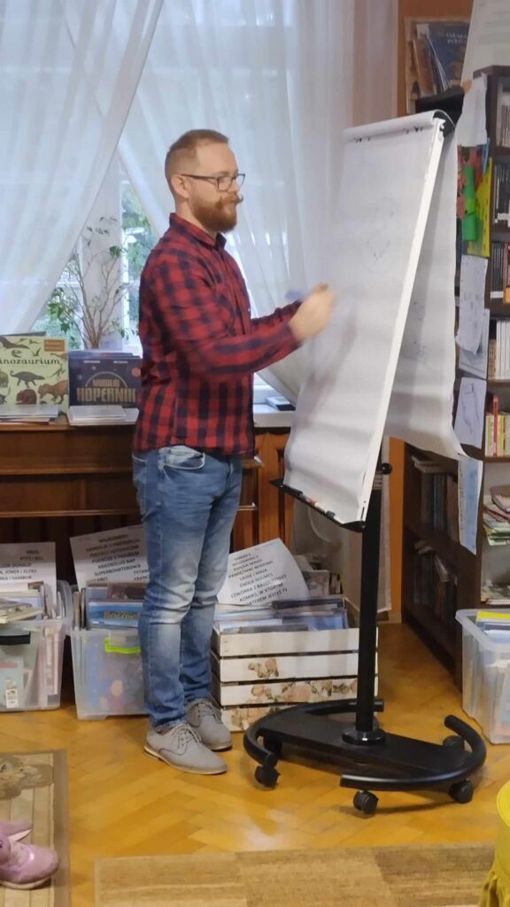Krzysztof Piersa pisze na białej kartce przymocowanej do przenośnej tablicy.