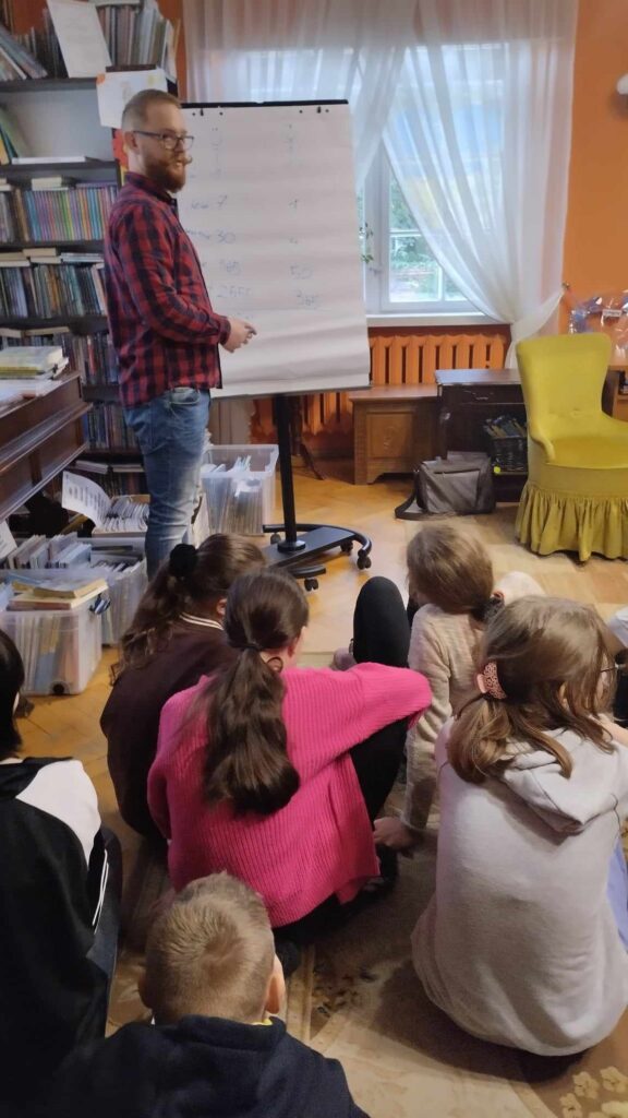 Krzysztof Piersa stoi przed siedzącą na dywanie młodzieżą.