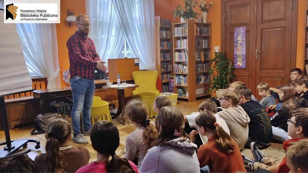 Krzysztof Piersa mówi do siedzącej na dywanie młodzieży.