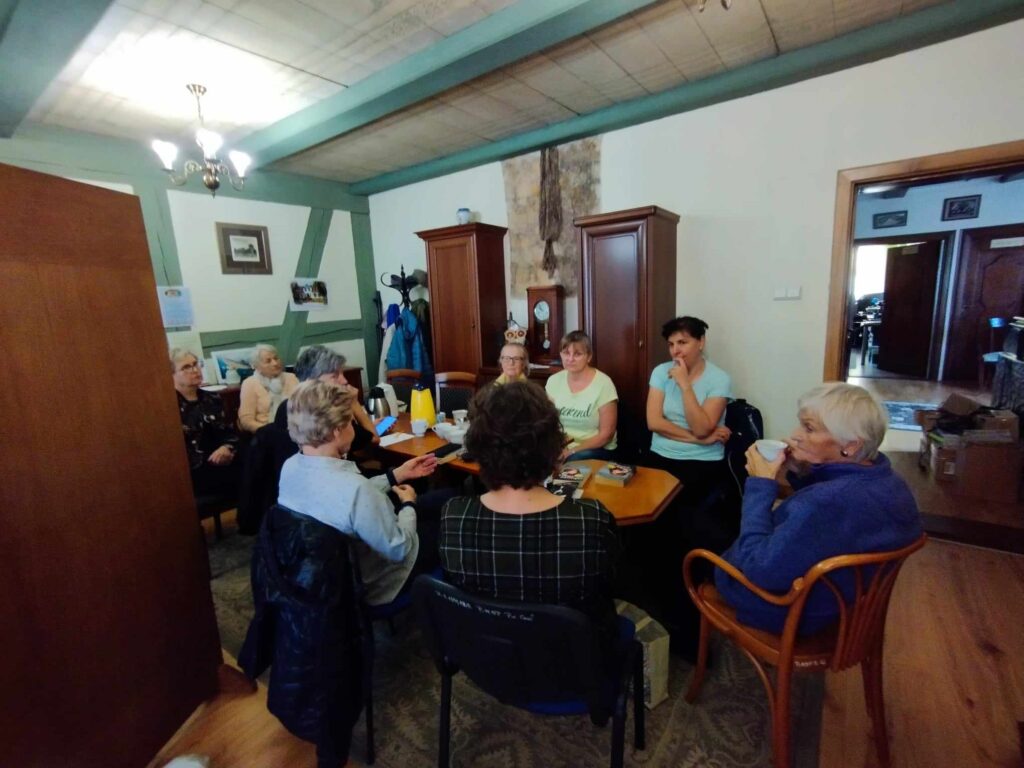 Członkinie Dyskusyjnego Klubu Książki siedzą przy stolikach, na których stoją filiżanki z kawą oraz leżą książki.