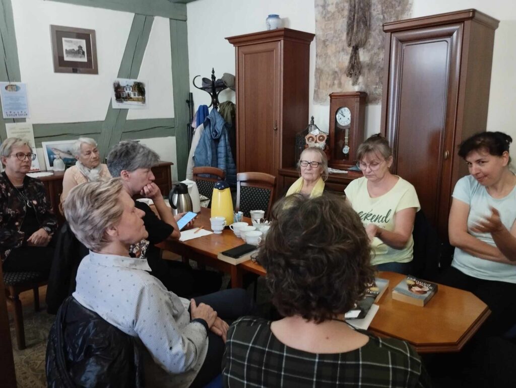 Członkinie Dyskusyjnego Klubu Książki siedzą przy stolikach, na których stoją filiżanki z kawą oraz leżą książki.
