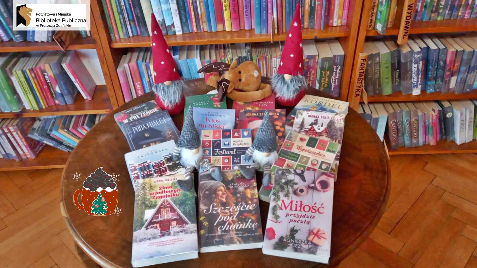 Na stoliku ułożone książki o tematyce świątecznej. Z tyłu, prawej i lewej strony, siedzą w czerwonych czapkach 2 skrzaty a pośrodku maskotka renifer.