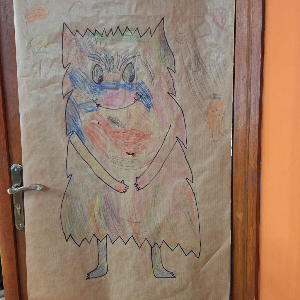 Kartka papieru. Na kartce narysowany jest kudłaty potwór pokolorowany różnymi kolorami. 
