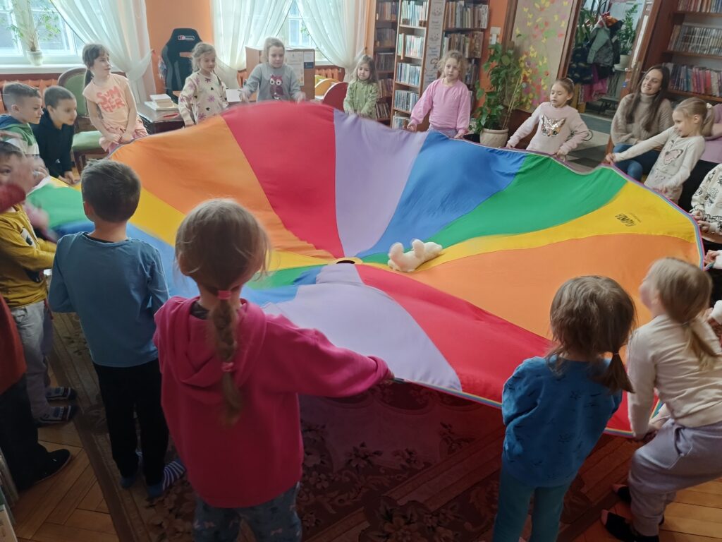 Dzieci zebrane w koło, trzymające za brzegi rozłożonej chusty animacyjnej.
