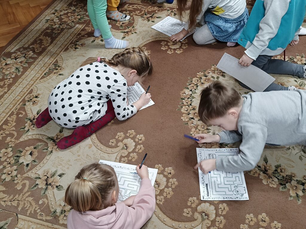 Kilkoro dzieci na dywanie. Próbują znaleźć rozwiązanie labiryntu. 
