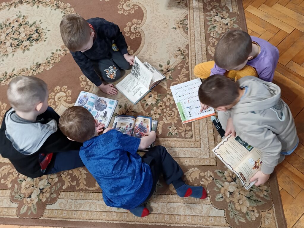 Pięciu chłopców siedzi na dywanie, każdy trzyma przed sobą otwartą książkę.