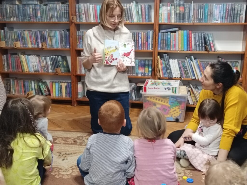 Bibliotekarka prezentuje książkę dzieciom.