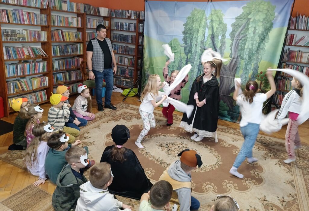 Dzieci w bibliotece podczas warsztatów teatralnych prowadzonych przez Sławomira Kochanka. Odgrywają sceny z Brzydkiego kaczątka.