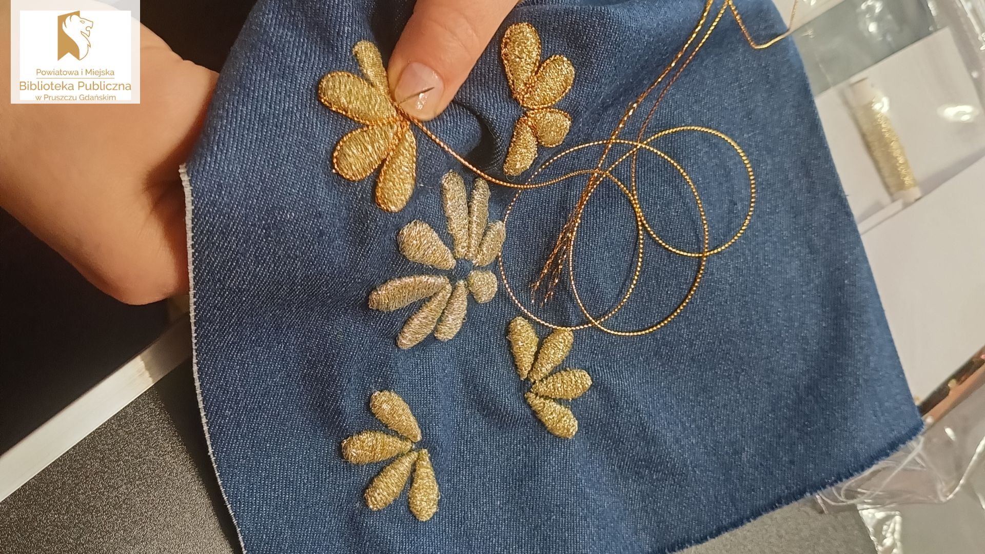 Płatki kwiatów wyszywane złota nitką na jeansowym materiale.
