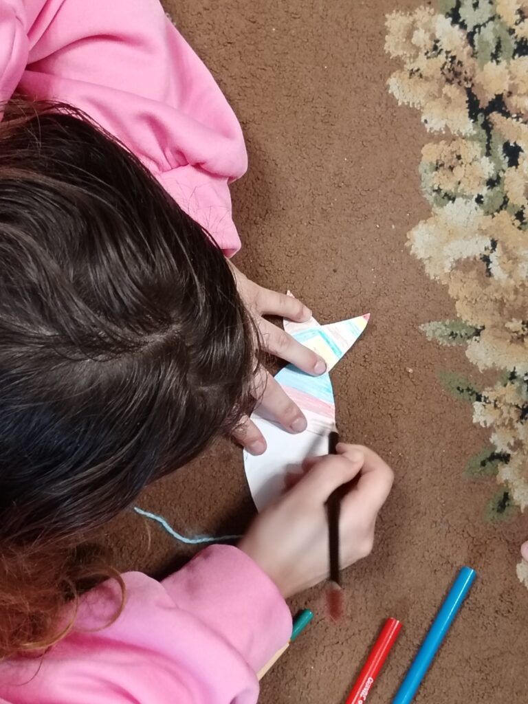 Dziecko kolorujące rybkę wyciętą z papieru.