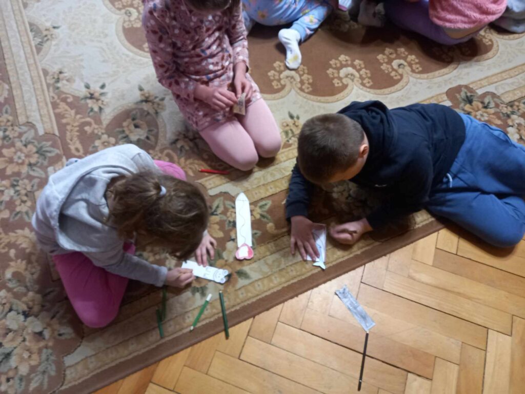 Troje dzieci siedzących na dywanie wykonuje zakładki do książki.