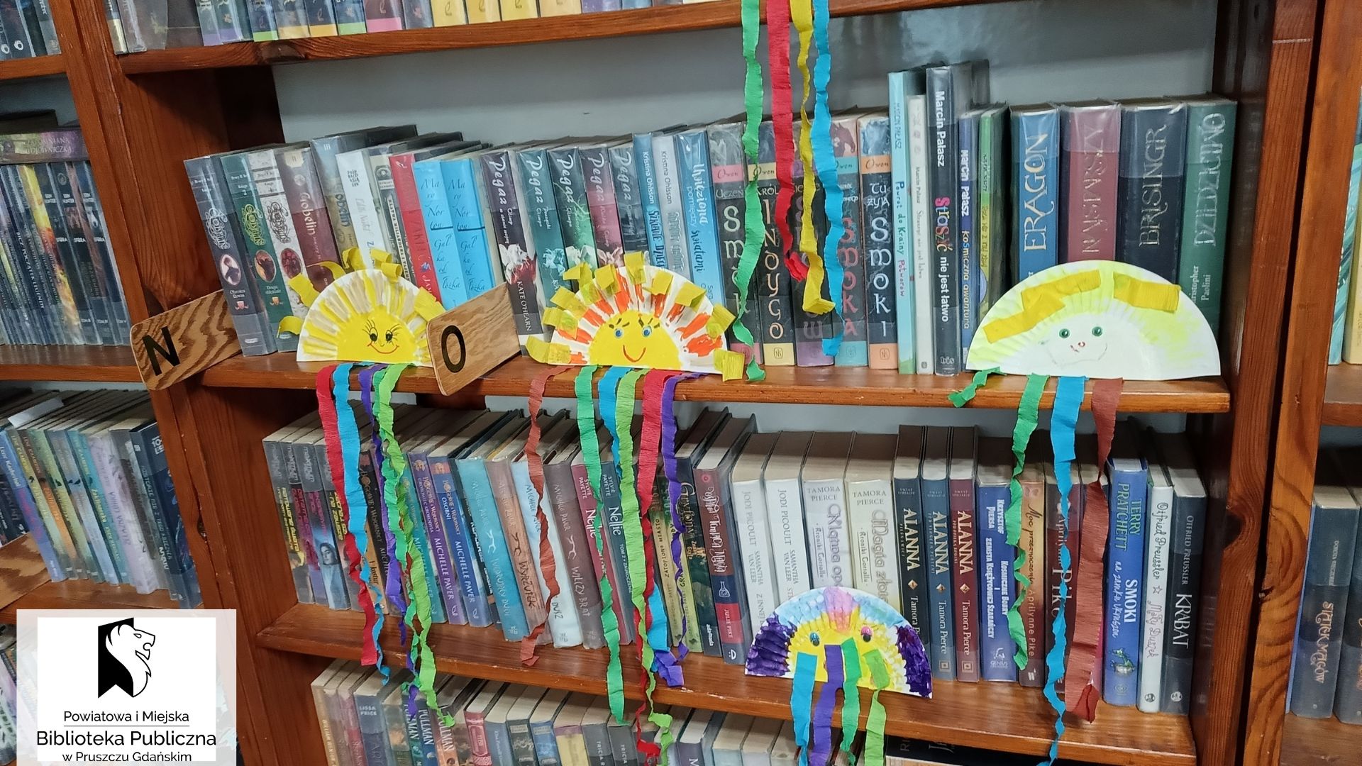 Prace plastyczne - słońca z papierowych talerzyków, ustawione na półkach z książkami.