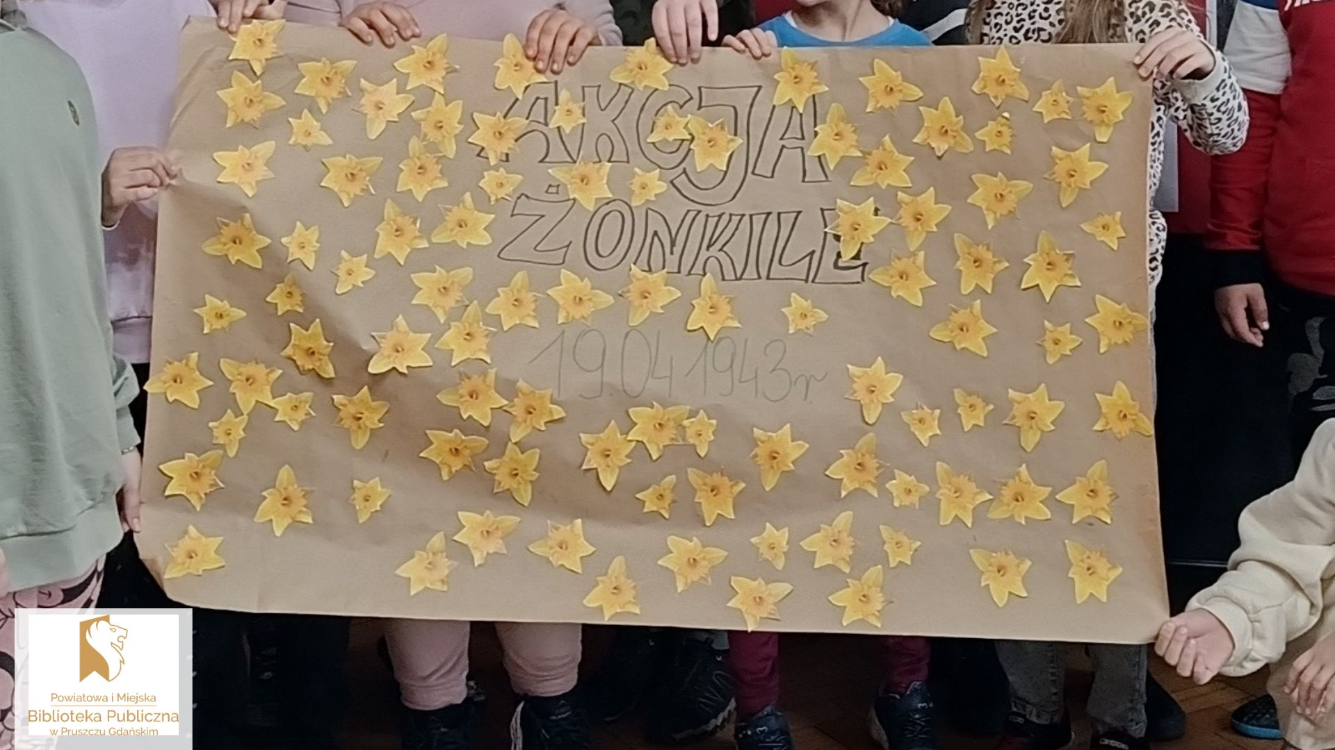 Arkusz szarego papieru z napisem Akcja Żonkile i przyklejonymi żółtymi kwiatami.