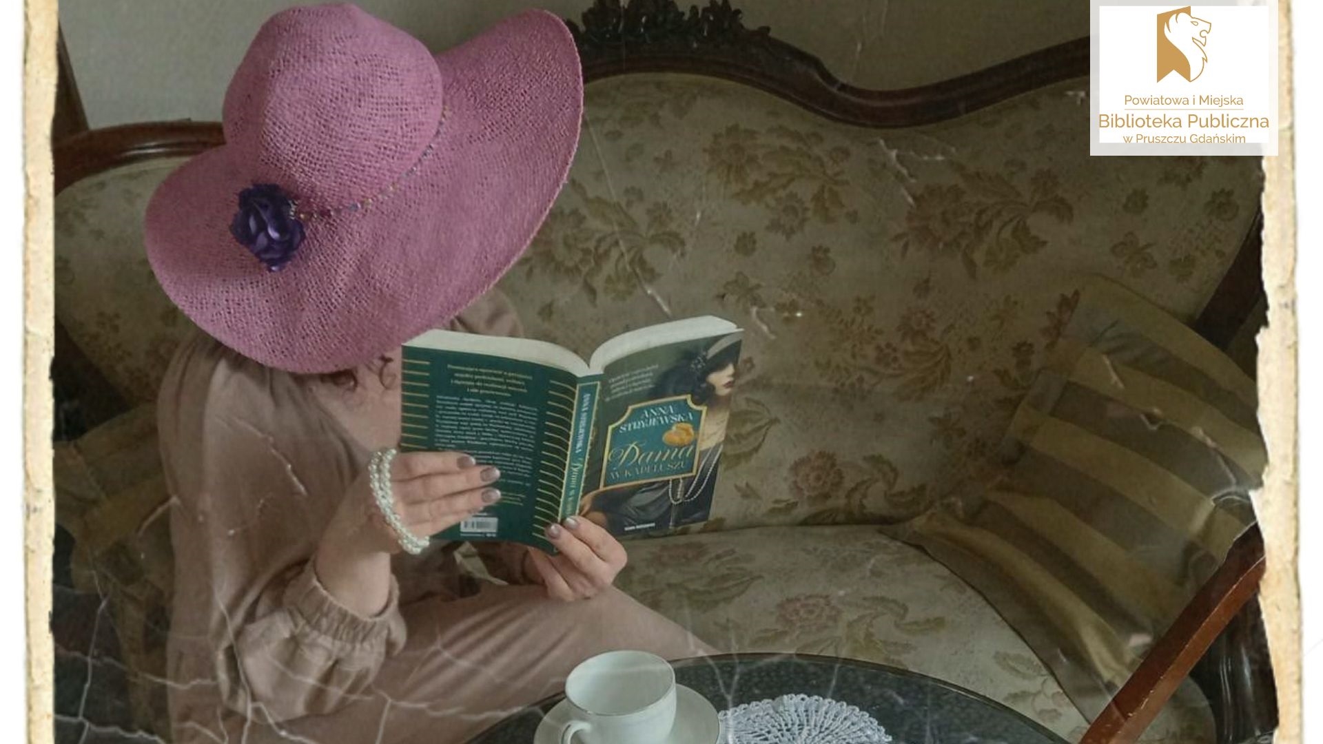 Kobieta w kapeluszu siedzi na antycznej sofie, w ręku trzyma otwartą książkę