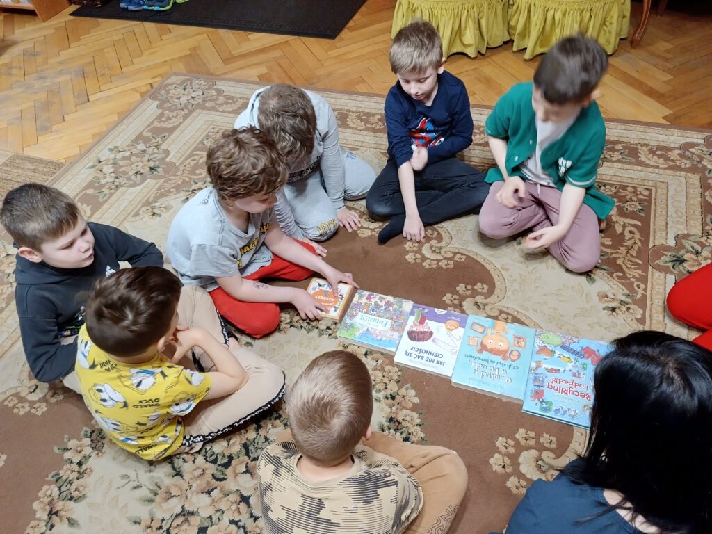 Chłopcy siedzą na dywanie. Układają książki według wielkości.
