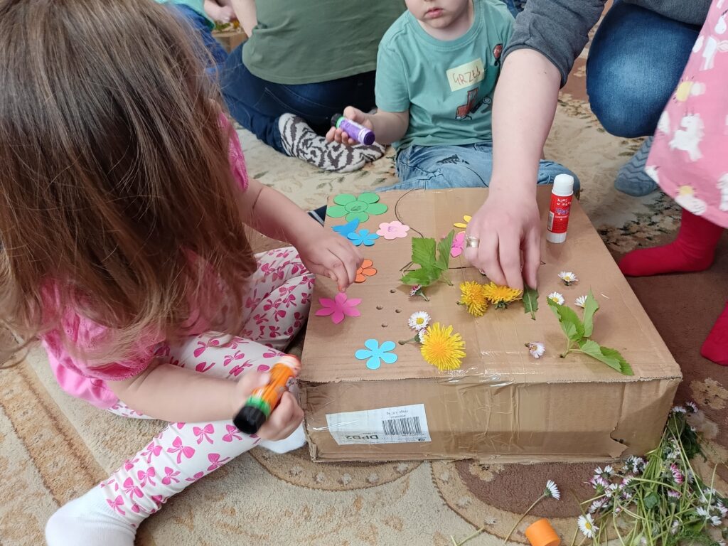 Dzieci ozdabiające kwiatami kartonowe wazony.