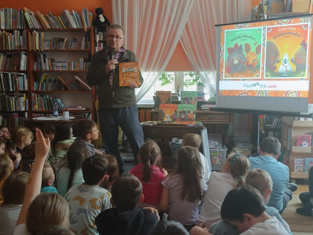 Marcin Kozioł prezentujący dzieciom swoją książkę. 