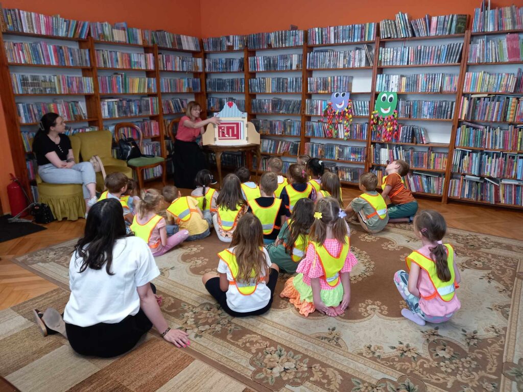 Bibliotekarka czyta teatrzyk kamishibai dzieciom siedzącym na podłodze.