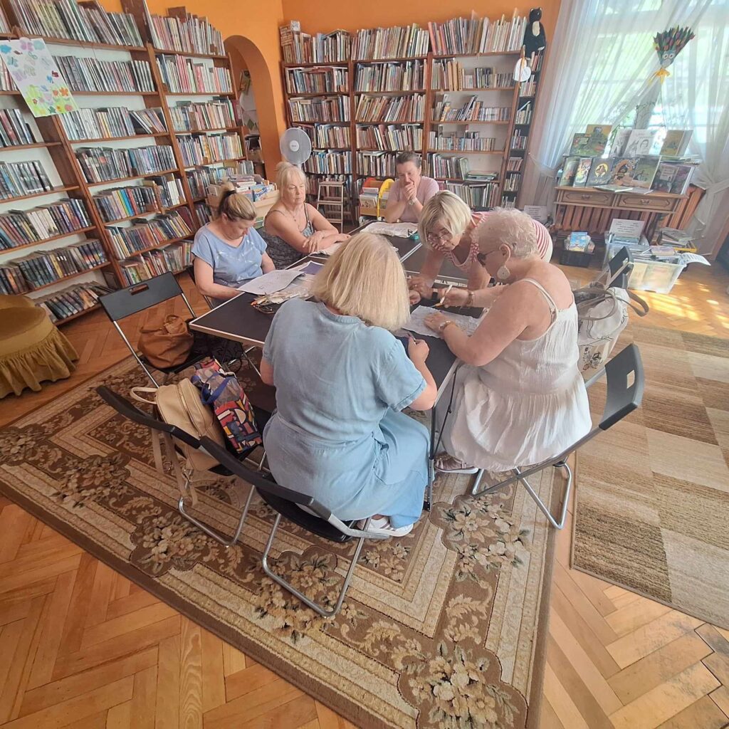 Sala biblioteczna. Przy stolikach siedzi 6 kobiet.