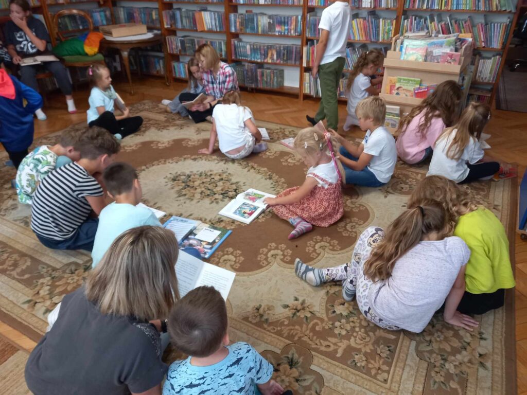 Sala biblioteczna. Na dywanie siedzą dzieci i oglądają książki.