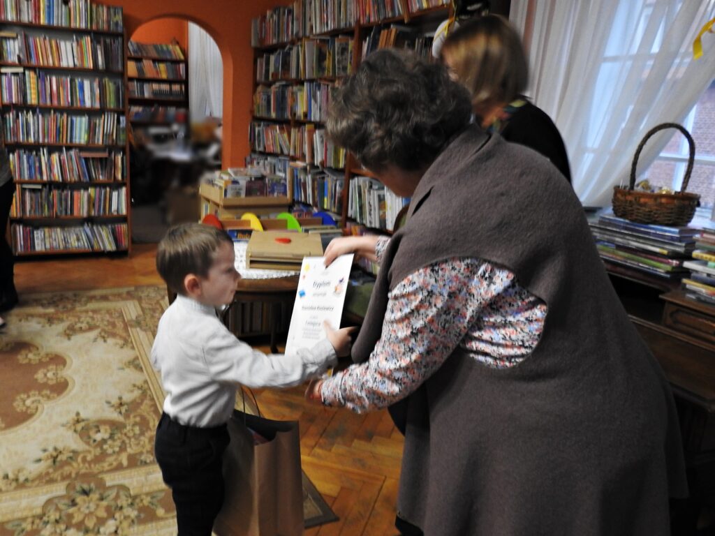 Bibliotekarka wręcza dyplom chłopcu. 