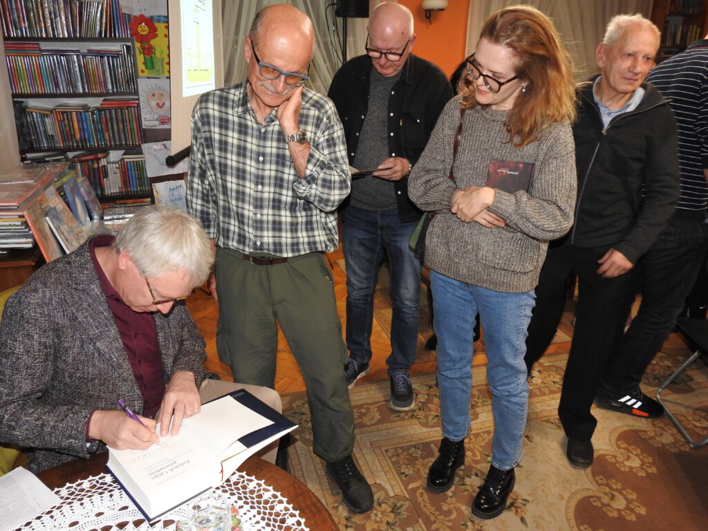 Peter Olivier Loew wpisuje autograf do książki. Obok Loeva stoją czytelnicy.